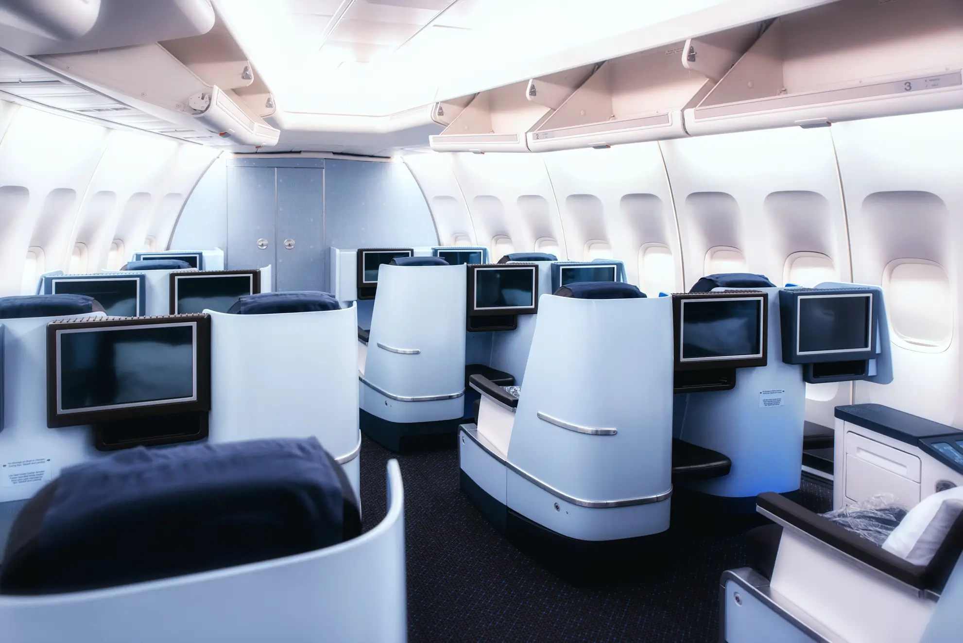 Interno cabina di prima classe su volo commerciale, con sedili reclinabili e schermi personali. Flyness, noleggio aerei e jet privati.