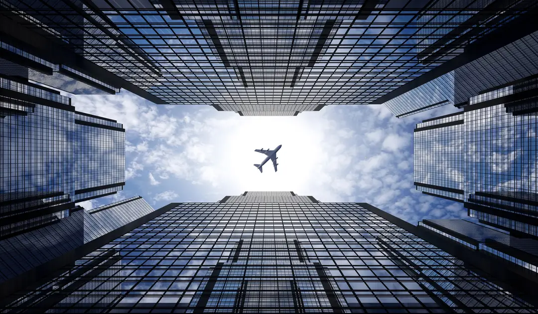 flyness from plan to plane Aereo in volo sopra grattacieli, a rappresentare il concept "From Plan to Plane" del servizio di noleggio aereo e jet privati Flyness.