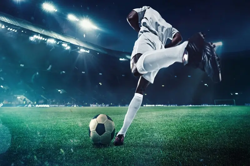 flyness voli privati trasferte sportive Calciatore calcia un pallone in uno stadio illuminato. Servizio di noleggio aereo Flyness per le trasferte di squadre sportive.