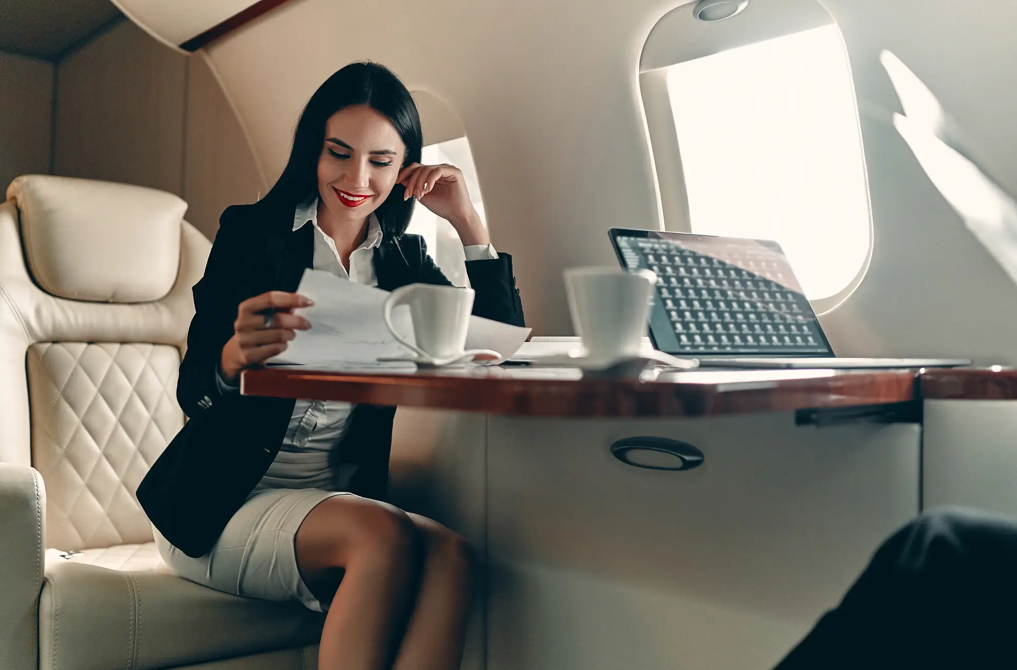 Donna manager lavora a bordo di un jet privato durante un volo business, tra documenti e laptop. Flyness, noleggio voli privati