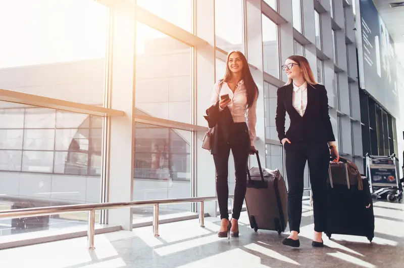 noleggio aereo charter viaggi incentive flyness Due donne camminano in un aeroporto con valigie per imbarcarsi su aereo charter privato per viaggio incentive. Flyness, air charter broker.