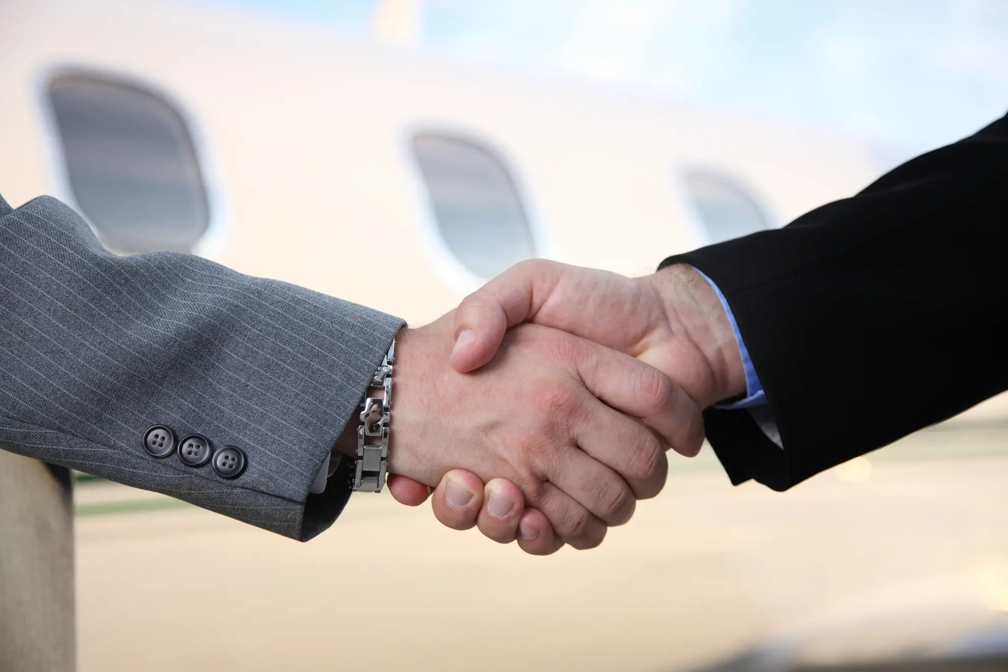 stretta-mano-flyness-successo-volo-charter Partner si stringono la mano davanti a un aereo: simbolo di fiducia e successo nel mondo dei voli charter Flyness per viaggi incentive.