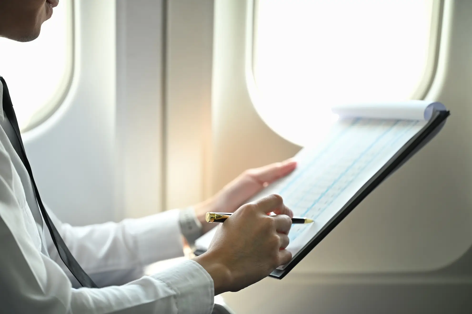 Dettaglio di una mano che compila una checklist durante un volo. Pianificazione operativa di una trasferta sportiva con Flyness.