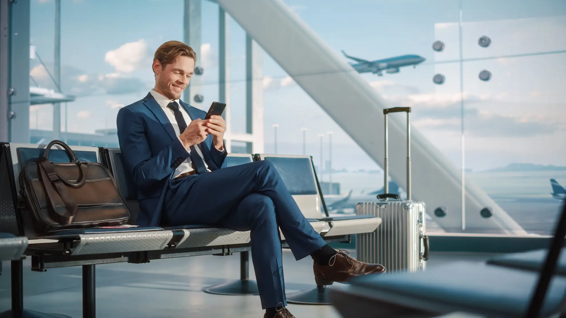 Professionista in aeroporto con smartphone, pronto a partire. Invito a contattare Flyness per organizzare trasferte sportive con voli charter.