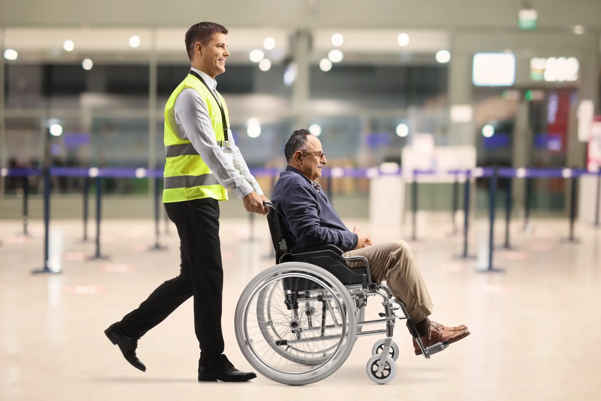 Addetto aeroportuale accompagna un pellegrino anziano in sedia a rotelle verso l'imbarco del volo, Flyness voli charter viaggi spirituali