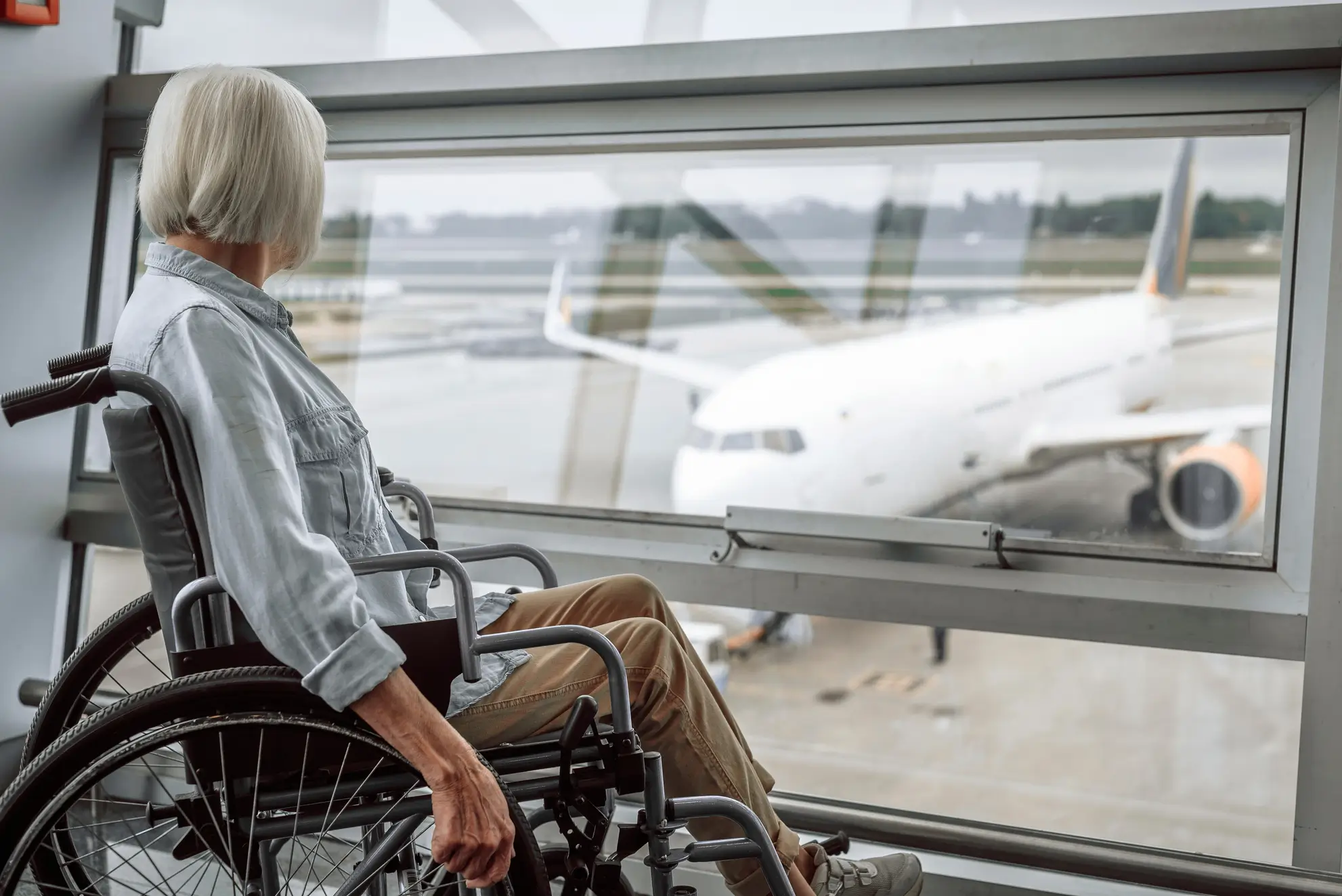 Donna anziana in sedia a rotelle osserva l’aereo in partenza: un viaggio spirituale con assistenza dedicata, Flyness air chartering
