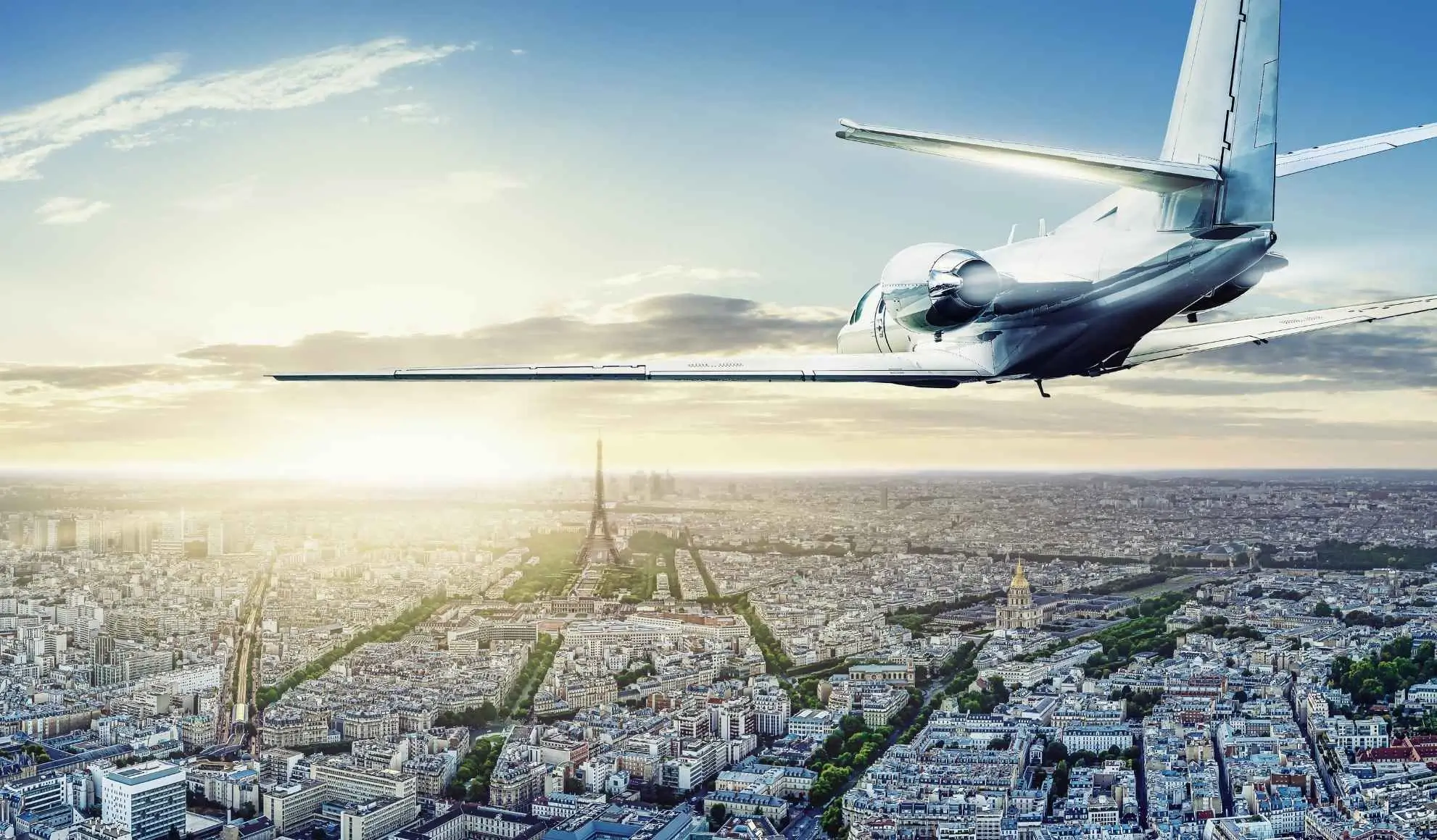 jet-privato-parigi-bleisure-travel-flyness Jet privato in volo sopra Parigi al tramonto con la Torre Eiffel sullo sfondo, simbolo di viaggio bleisure Flyness
