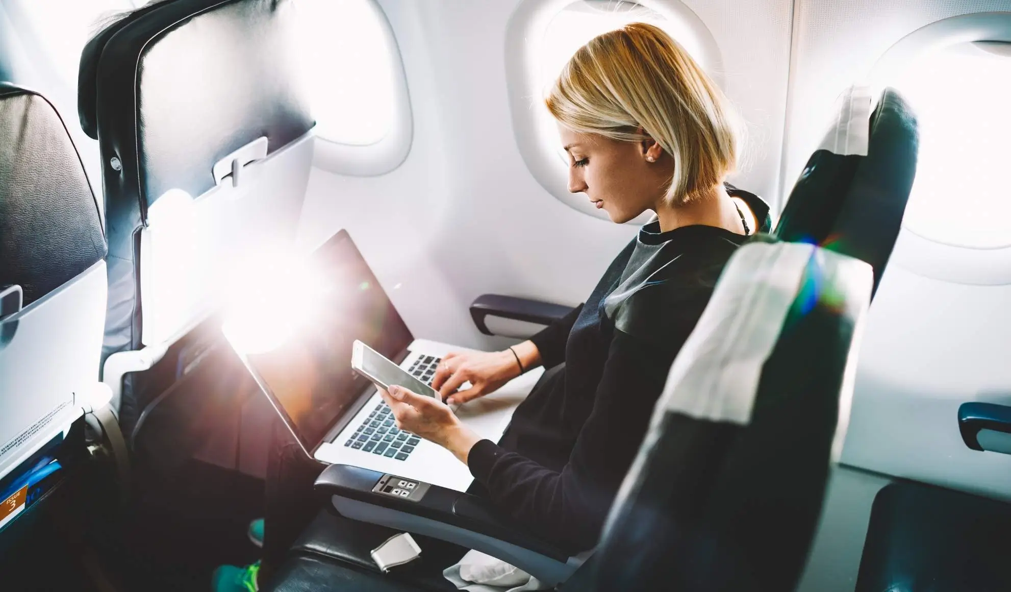 wifi-in-aereo-laptop-smartphone Passeggera usa laptop e smartphone con Wi-Fi in cabina, simbolo delle nuove tecnologie di connessione in aereo 2025-26