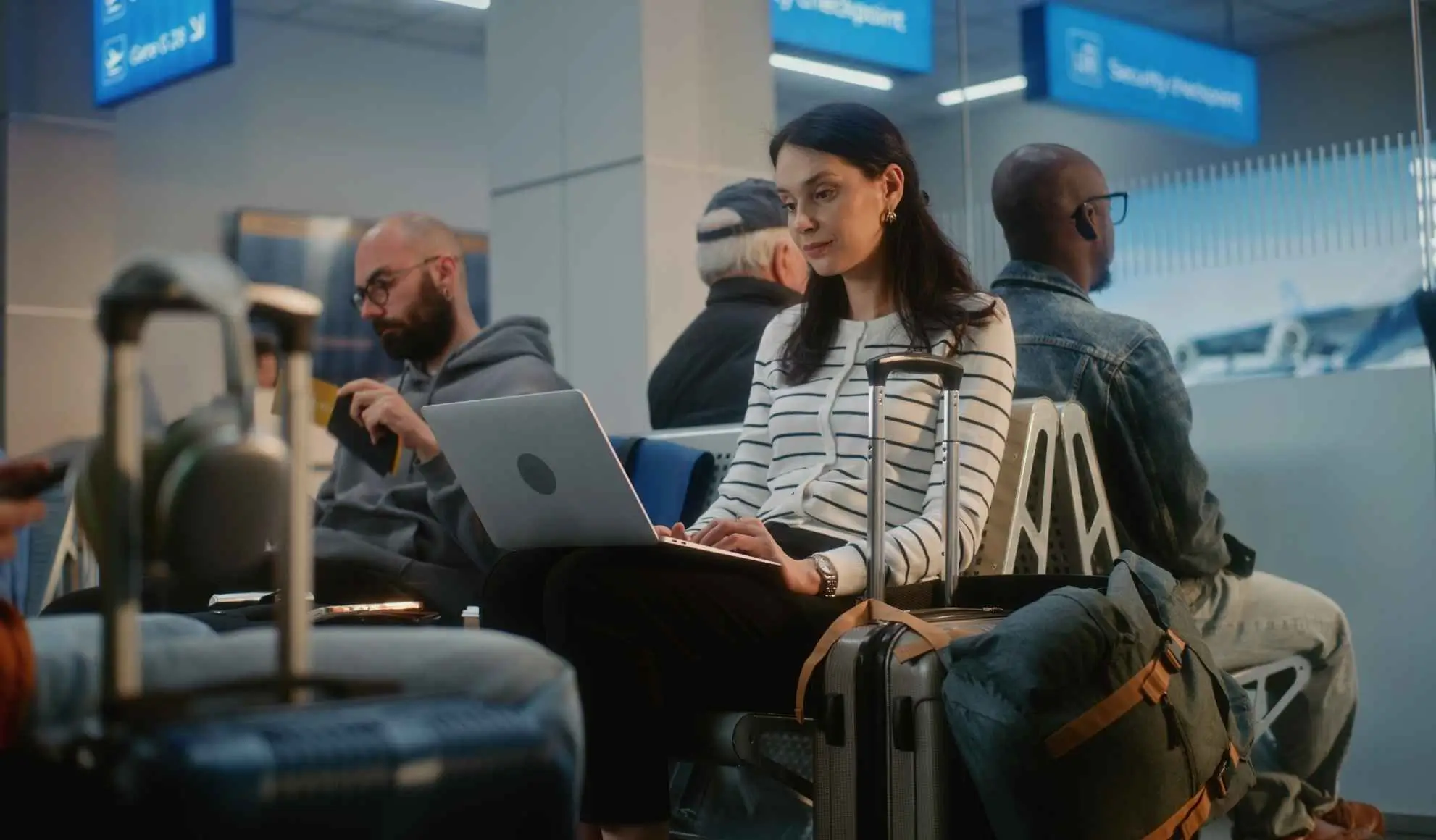 voli-combinati-attese-organizzazione-viaggi-di-lavoro Donna seduta che lavora con laptop sulle ginocchia, in attesa in aeroporto durante voli combinati nei viaggi di lavoro