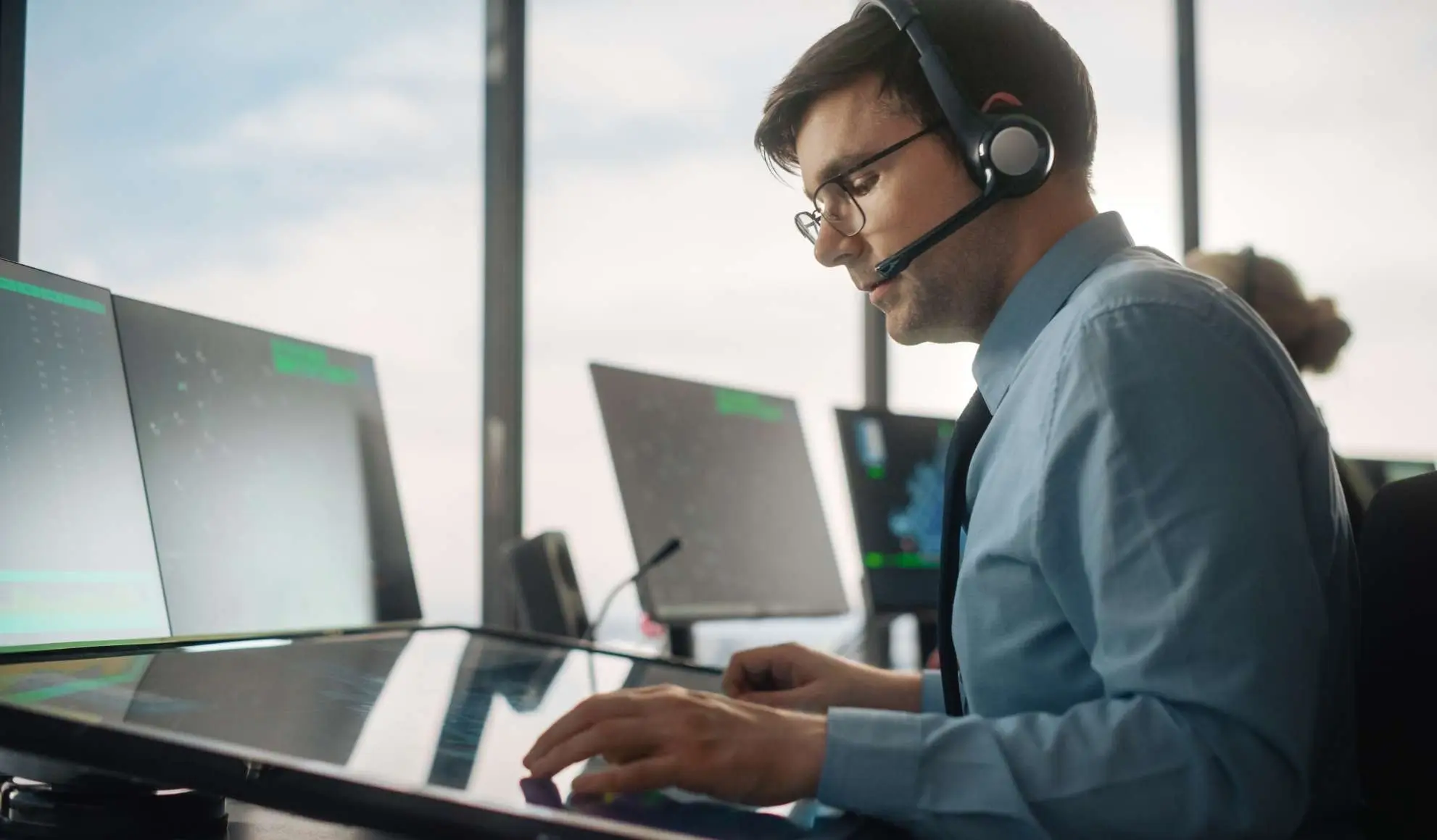 Operatore di volo seduto a una postazione con cuffia e più schermi che mostrano dati operativi, simbolo del metodo Flyness di gestione voli.