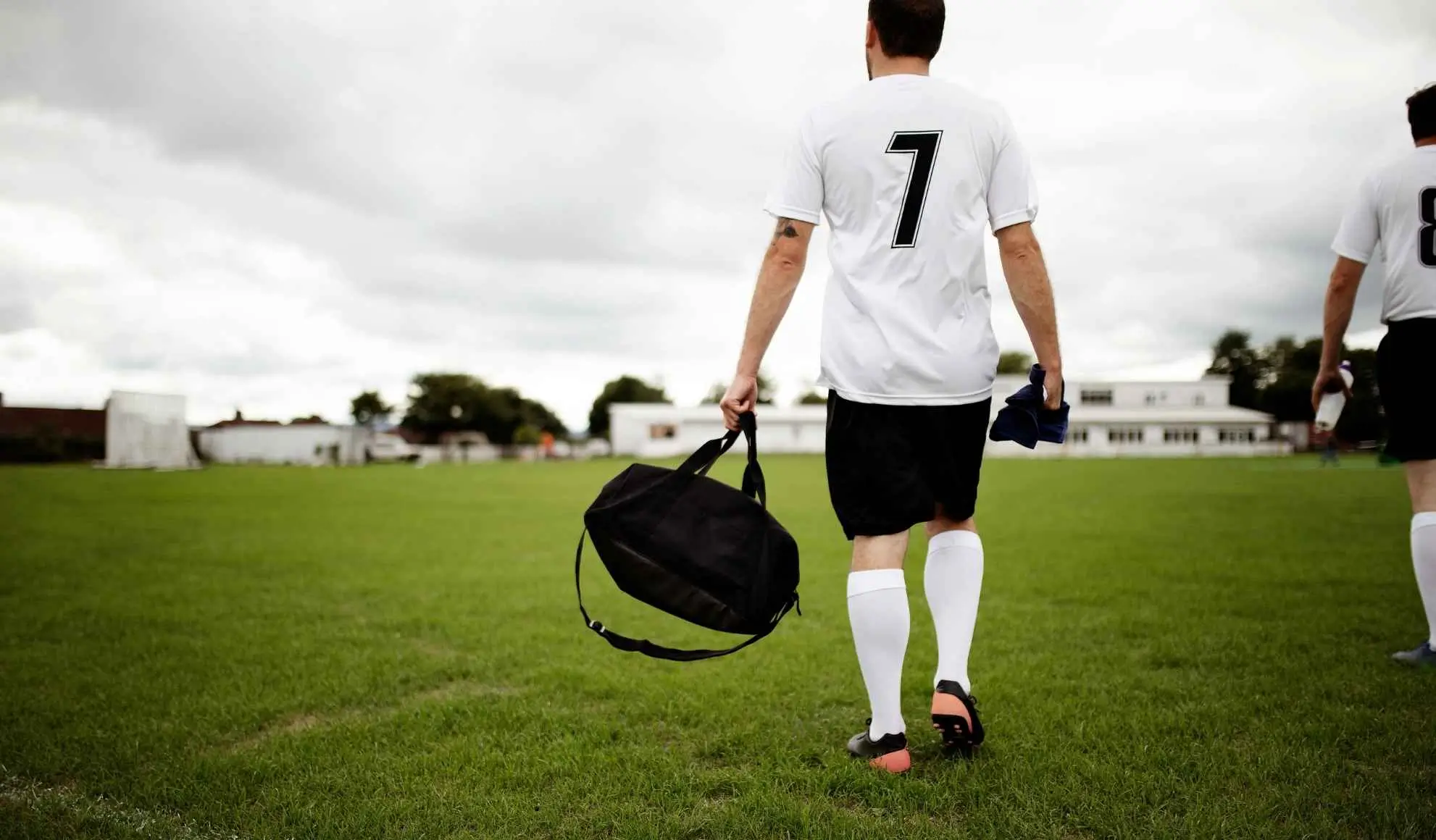 ritiri-estivi-calcio-arrivo-campo-preparazione Giocatore di calcio con borsone che entra in campo durante fase iniziale di ritiro estivo
