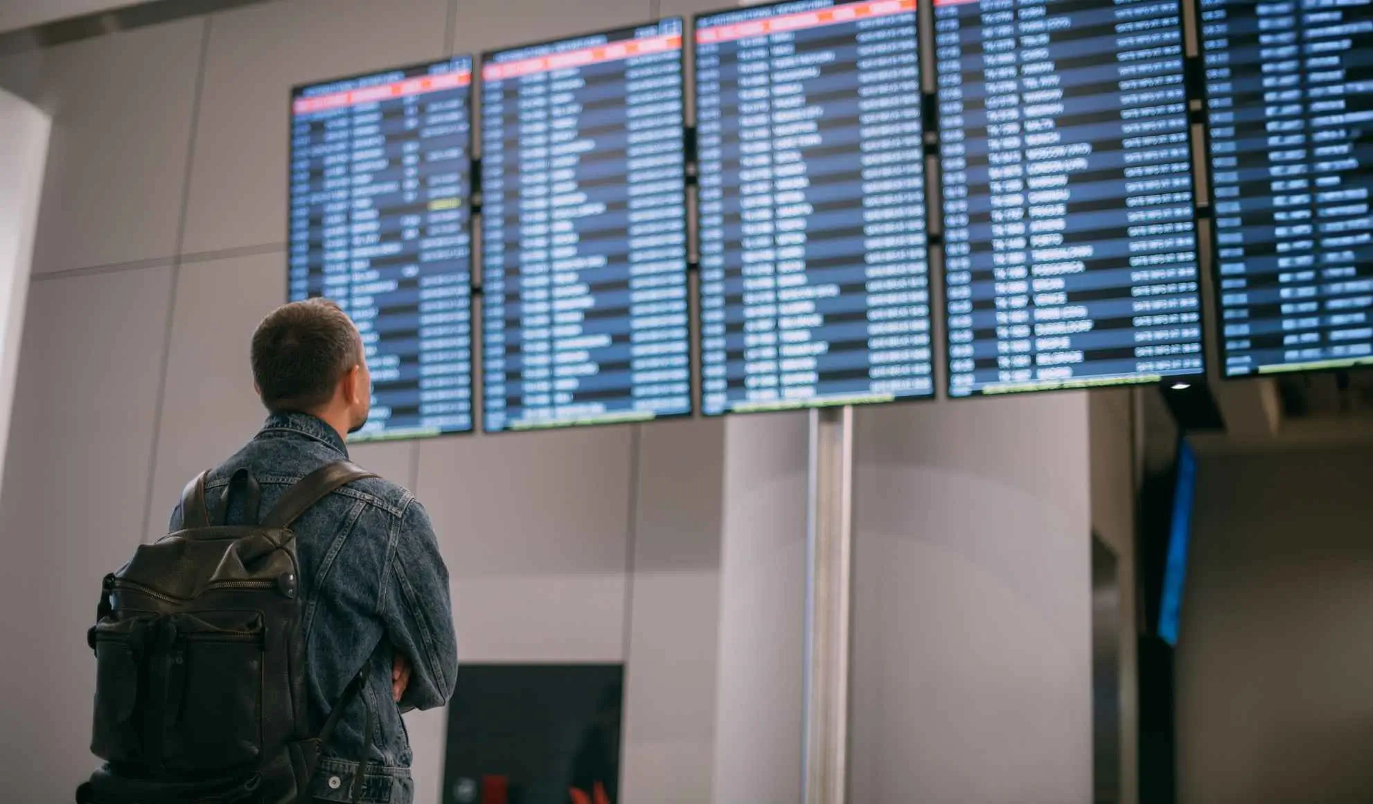 sigle-aeroportuali-tabellone-partenze-aeroporto Viaggiatore davanti al tabellone partenze in aeroporto con sigle aeroportuali e codici aeroportuali per identificare voli e destinazioni