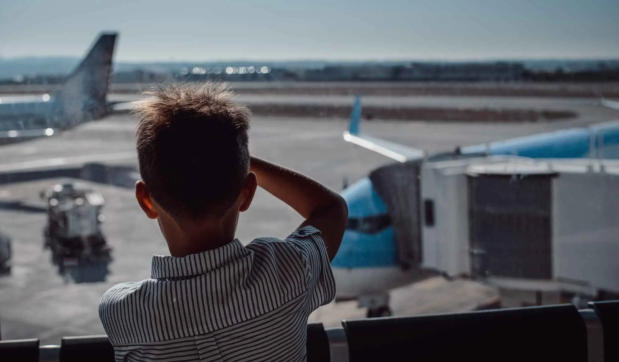 Bambino osserva un aeromobile attraverso la vetrata di un aeroporto