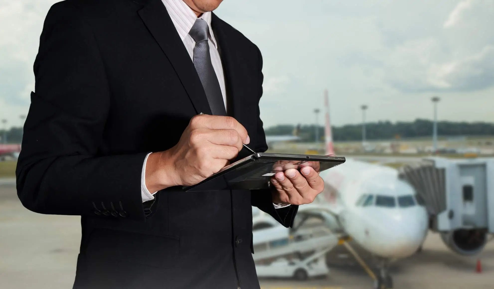 Professionista aviation consulta un tablet in aeroporto per valutare disponibilità, costi e pianificazione di un volo charter Flyness