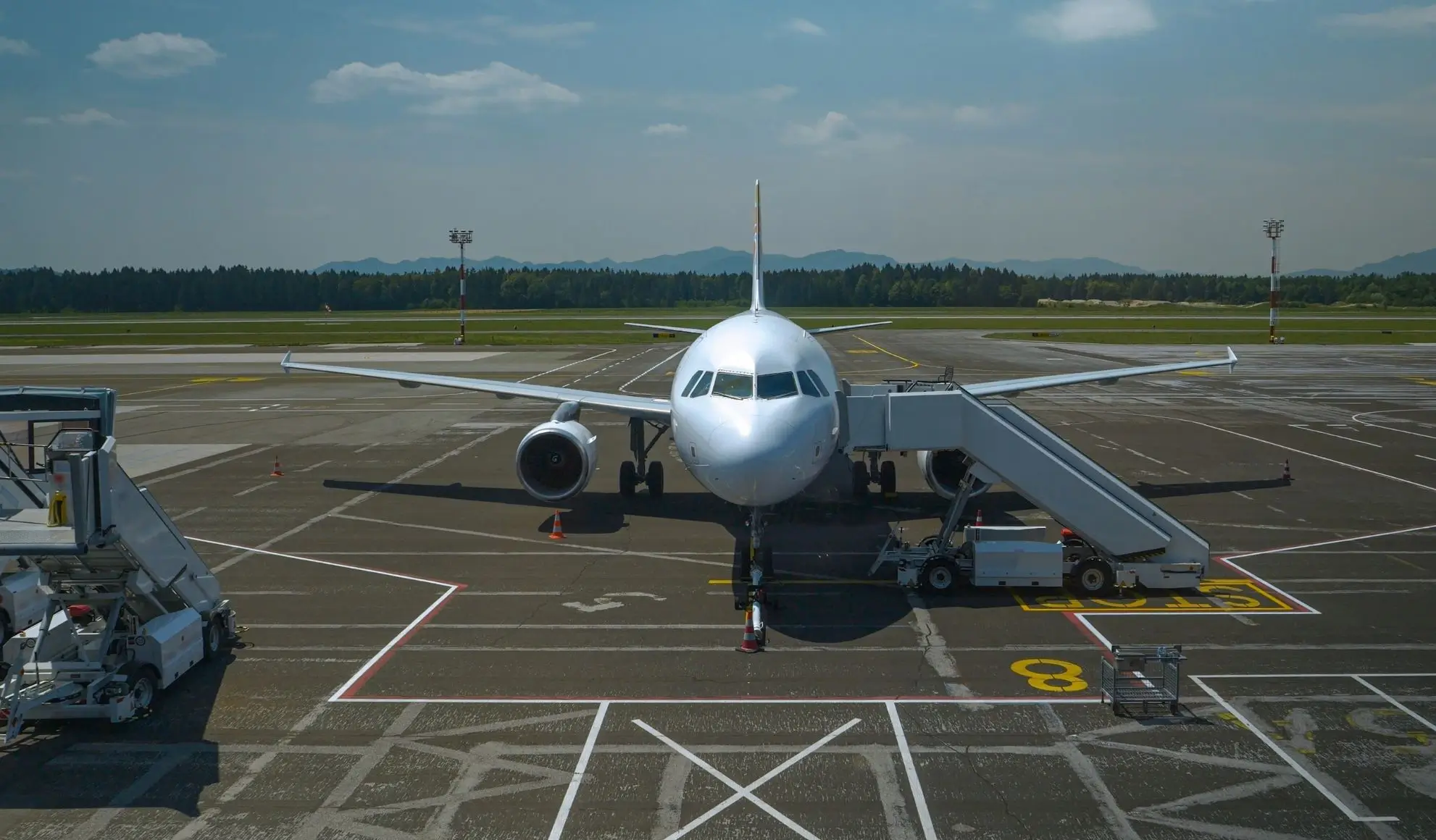 servizi-handling-aeroportuale-aeromobile-piazzale Aeromobile in sosta sul piazzale con scala e mezzi per i servizi di handling aeroportuale.